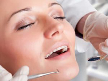 Head-only photo of a young woman with her eyes closed and smiling as dental tools are being held near her mouth; for information on how Sugar Land dentist Siny Thomas caters to cowards.