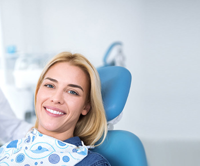 Blonde woman in sitting in a dental chair smiling after root canal treatment.