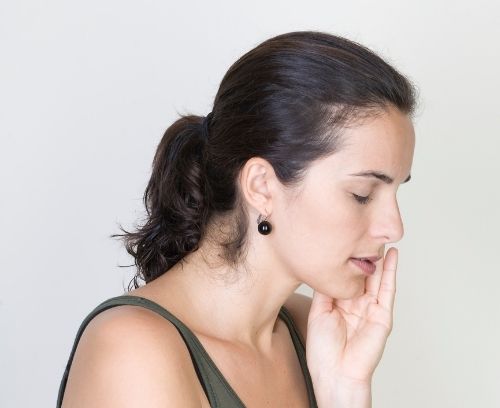 Brunette woman holding the side of her face - portraying tooth sensitivity